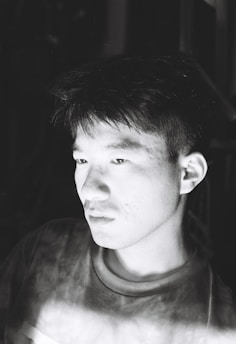 A candid black and white portrait of an artist deep in thought, surrounded by their artwork in a minimalist studio.