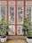 A decorative wooden panel featuring intricate carvings of animals and floral designs. The panel consists of four sections, each adorned with detailed artwork. In front, two potted plants with green foliage are placed symmetrically. The pots are white with blue artistic patterns.