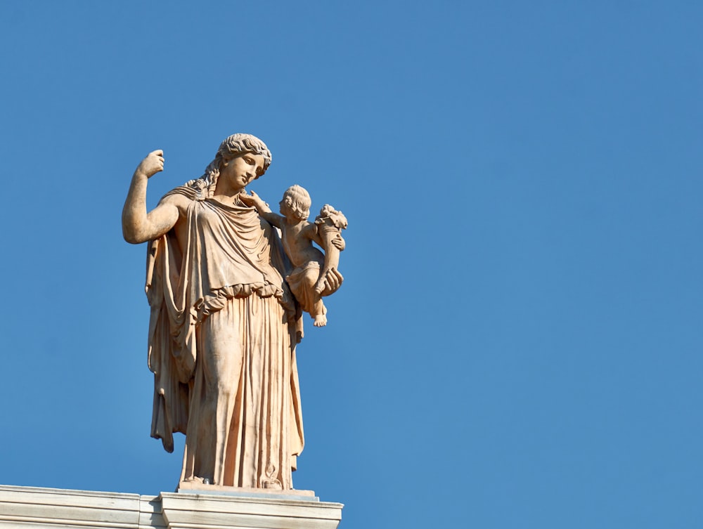 eine Statue einer Frau, die ein Kind auf dem Dach eines Gebäudes hält