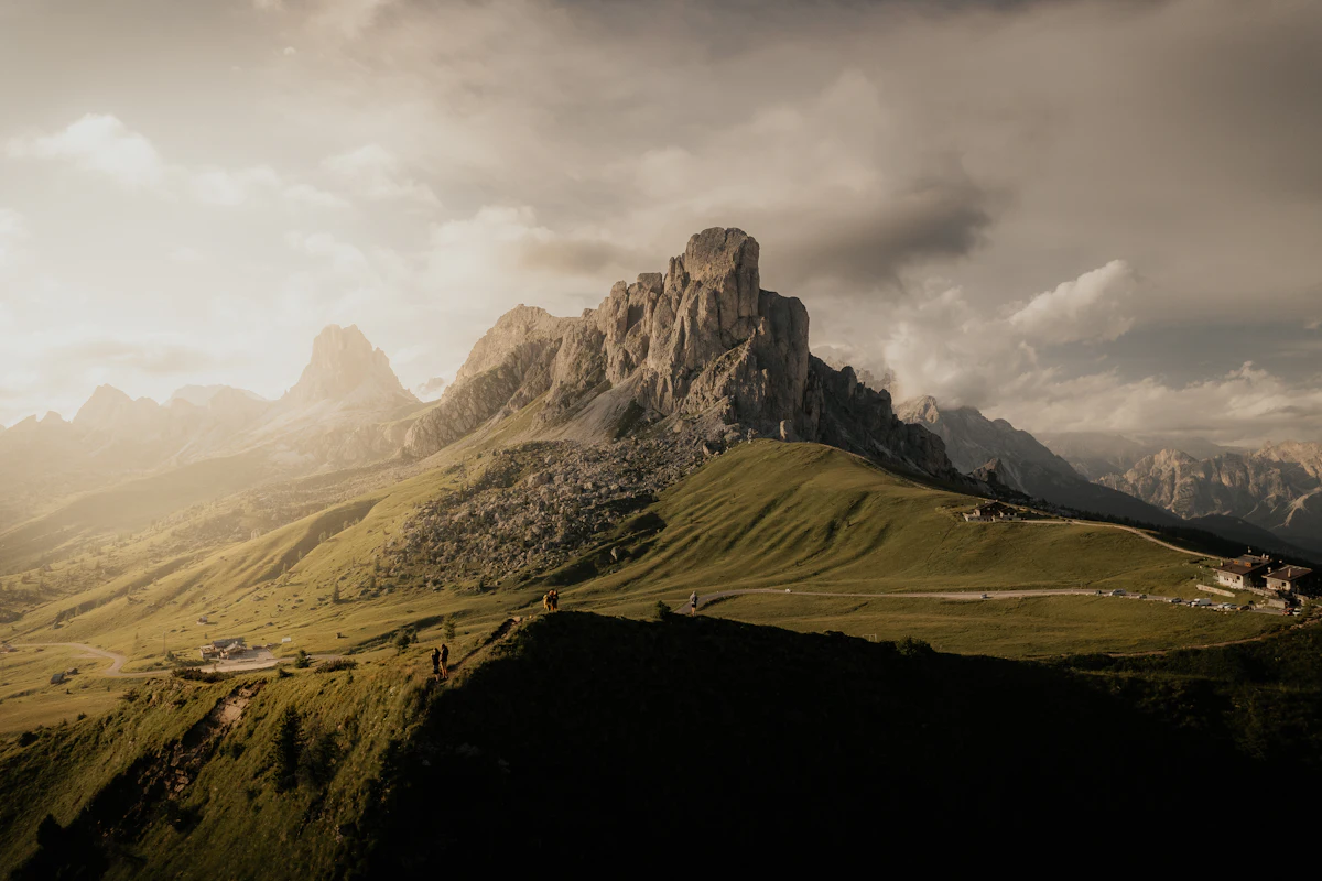 Grassy slopes and a road at Passo Giau below a rock tower, in evening light