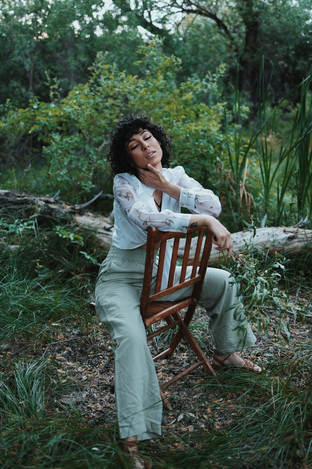 a woman sitting on a wooden chair in the woods