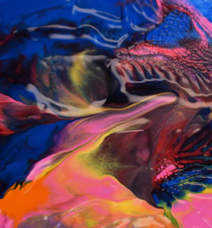 A vibrant and abstract blend of swirling colors, including deep blues, bright pinks, warm yellows, and vivid oranges creating a dynamic and fluid pattern. The image features organic shapes and textures that evoke a sense of movement and energy.