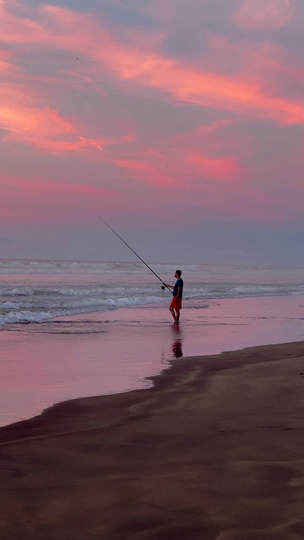 a man fishing on the beach at sunset