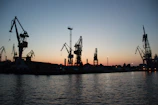 Evening scene showing cranes silhouetted against the sky as they complete a complex lift.