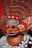 A highly ornate and colorful traditional costume featuring a mask with intricate designs and patterns. The headpiece and collar are elaborately decorated with metallic details and rich, textured materials. The colors are predominantly red and orange, with accents of white and silver. The overall appearance is ceremonial and artistic, indicative of cultural or ritualistic significance.