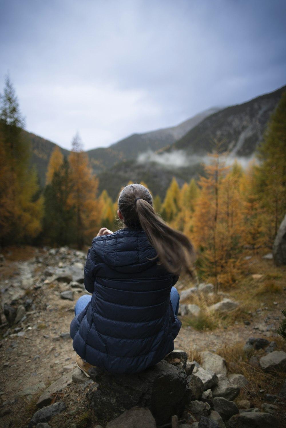 a woman sitting on a rock looking at the mountains