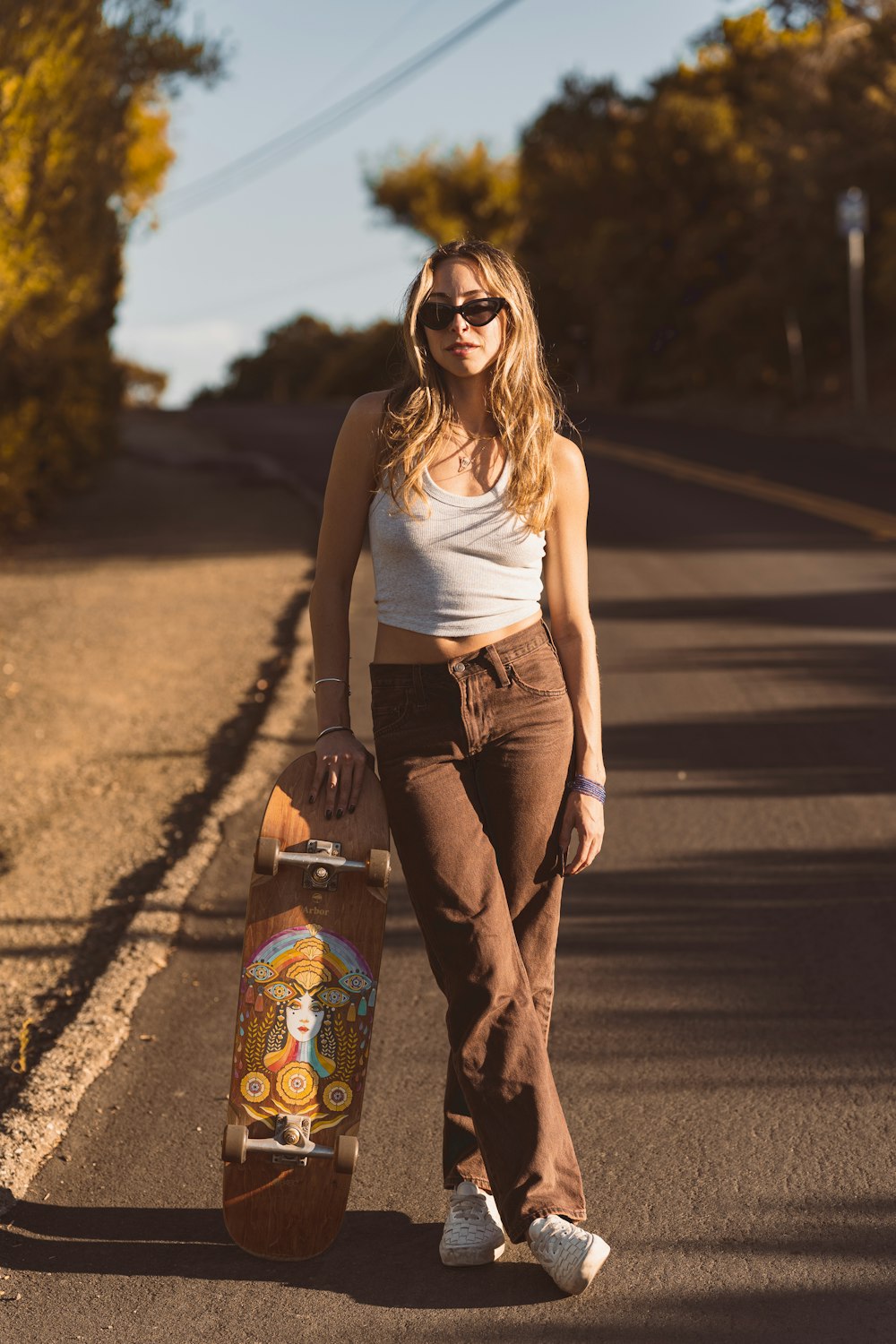 a woman holding a skateboard on the side of a road