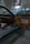 The interior of a luxury car showroom features an open car door with brown leather and fabric upholstery. Bright showroom lights illuminate the sleek design, while large windows allow natural daylight to stream in. A framed photograph of a blue sports car is displayed on the wall above.