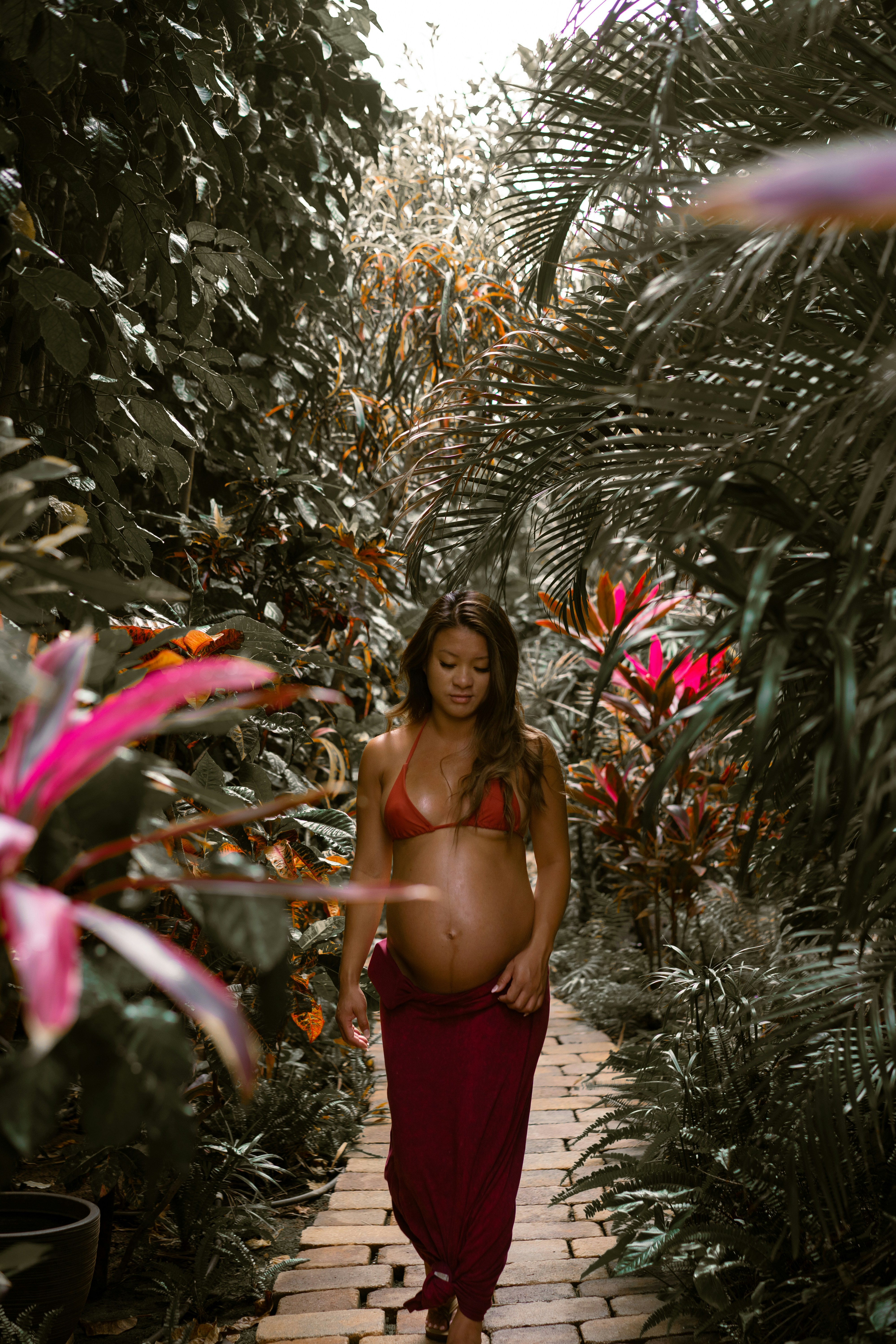 a pregnant woman in a red bikini walks down a path