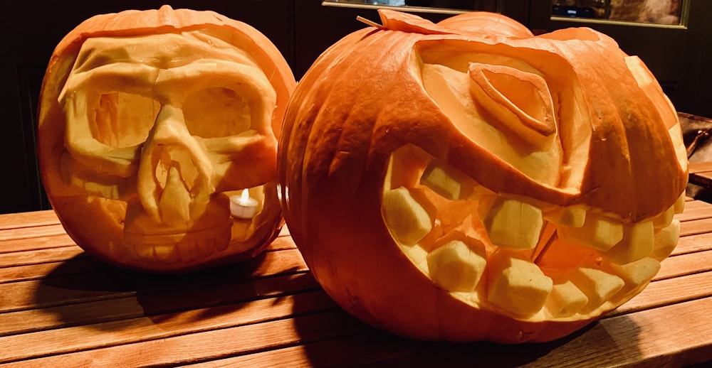 two carved pumpkins sitting on top of a wooden table