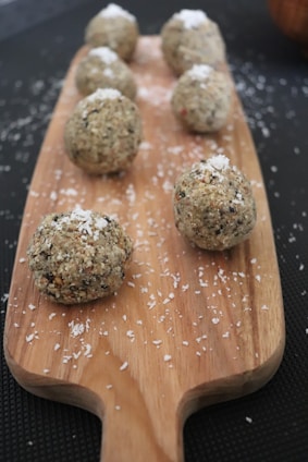 Close-up of freshly made laddus arranged on a rustic wooden board with scattered dry fruits and seeds around.