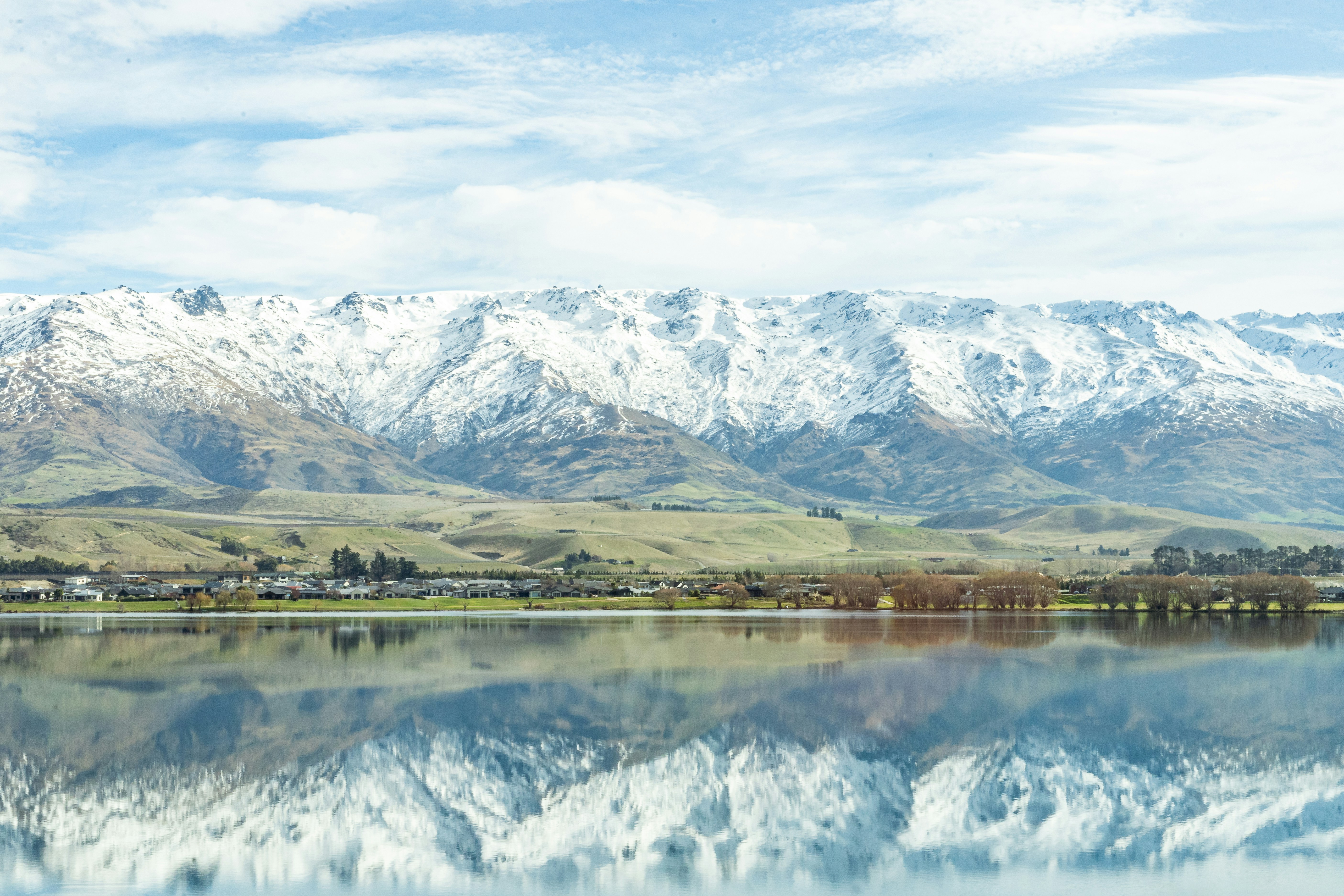 a large body of water surrounded by mountains, View of snowy Mt Pisa and its reflection on Clutha River/Mata-Au (Lake Dunstan).