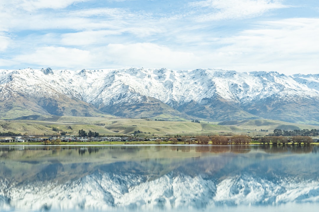 a large body of water surrounded by mountains, View of snowy Mt Pisa and its reflection on Clutha River/Mata-Au (Lake Du