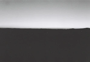 A minimalist, cinematic frame of a single subject silhouetted against a softly glowing horizon.