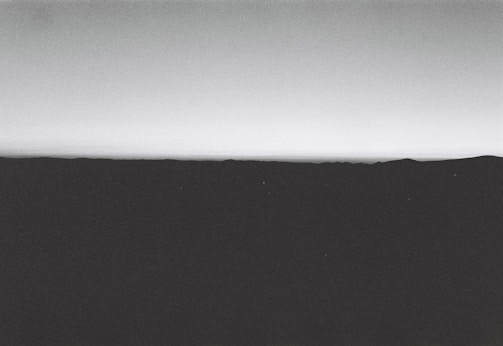 A minimalist and monochrome landscape with a horizon line that separates the dark foreground from the lighter sky.