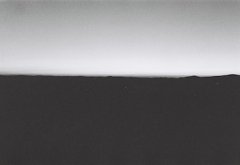 A minimalist and monochrome landscape with a horizon line that separates the dark foreground from the lighter sky.