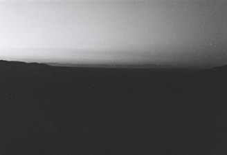 A grayscale landscape capturing a vast and quiet scenery with a dark foreground and a gradient sky.