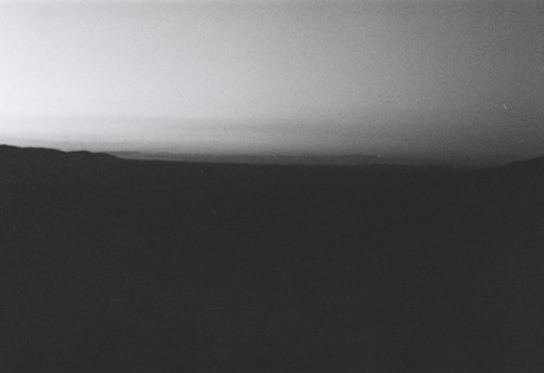 A grayscale landscape capturing a vast and quiet scenery with a dark foreground and a gradient sky.