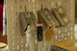 Ceramic cat-shaped utensils rest in a glass, featuring varying designs and colors. In the background, products hang on hooks against a perforated display board.