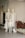 A display of four white mannequins, two adults and two children, are dressed in light-colored outfits with soft, pastel patterns. They are positioned next to a potted plant with red and green leaves, and a small white ceramic dog sculpture is placed beside them.