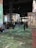 A large indoor exhibition space with projections of colorful floral and abstract patterns on walls and floors. The room is filled with people, some sitting and others walking, engaging with the immersive art experience. Tall metal columns are present, supporting the structure.