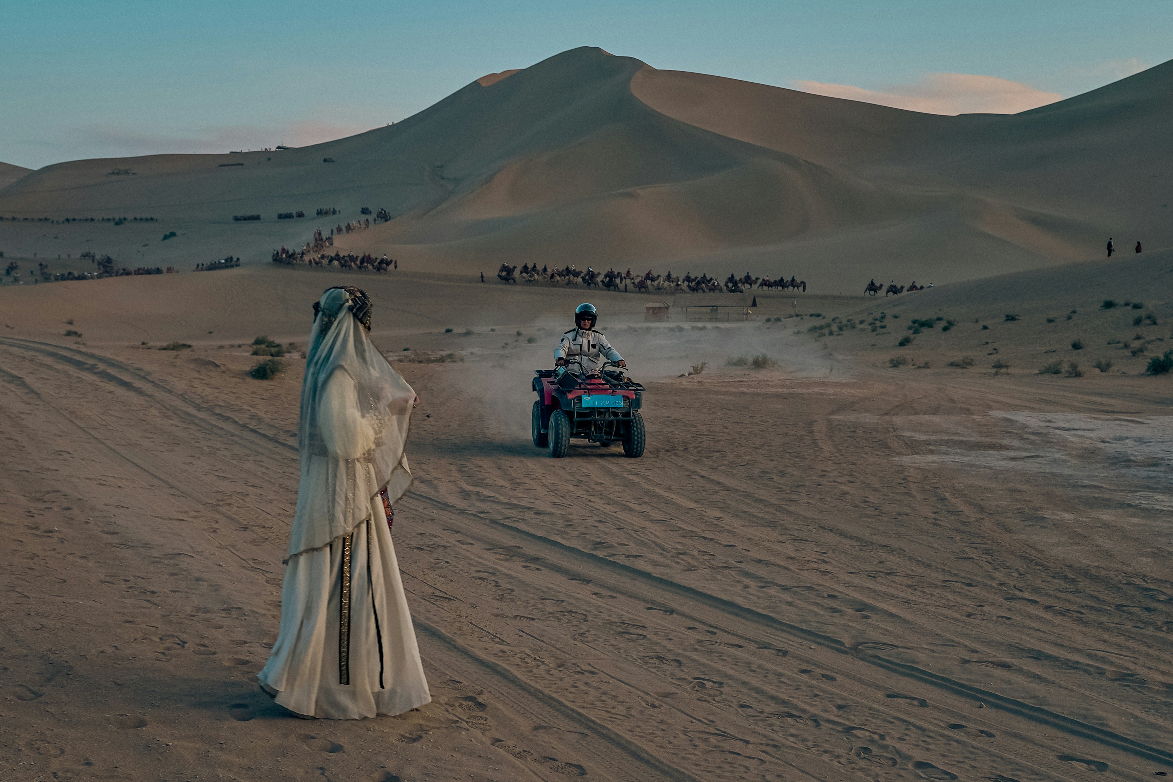 Person rides atv in desert with distant caravan