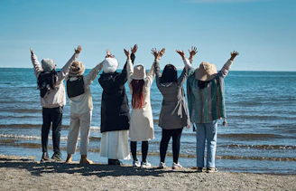 Seven people with arms raised on a beach