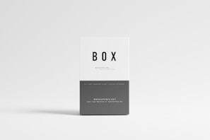 A minimalistic box with a clean white and gray design. The box is labeled with the word 'BOX' in bold black letters on the upper portion, and more text in smaller font is seen below. The background is light gray, creating a simple and modern aesthetic.