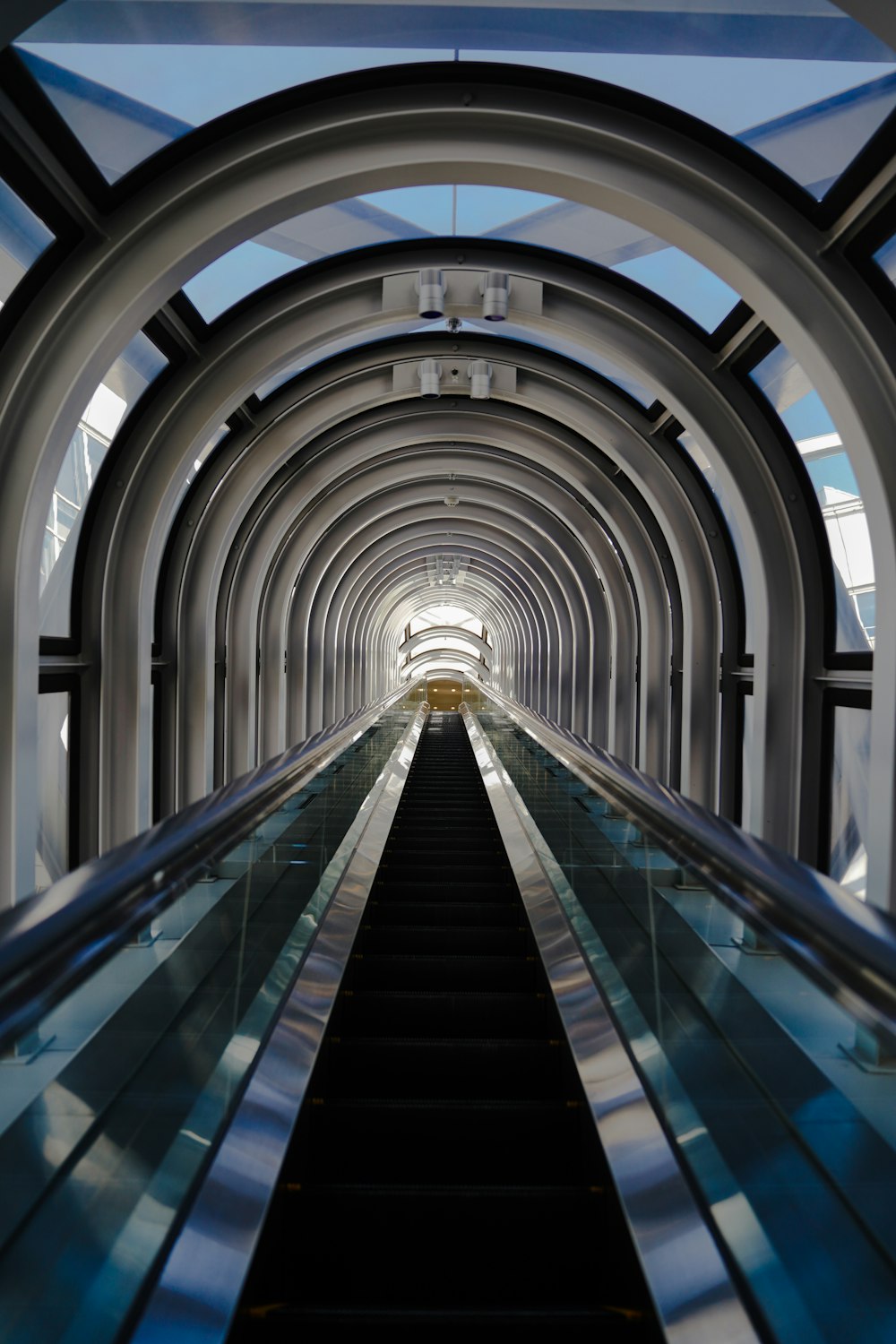 uma escada rolante descendo um túnel com um fundo de céu