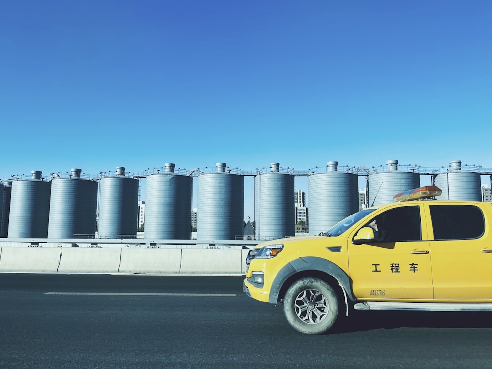 a yellow pick up truck parked in front of a row of silos
