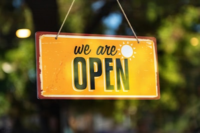 a yellow sign that says we are open hanging from a string