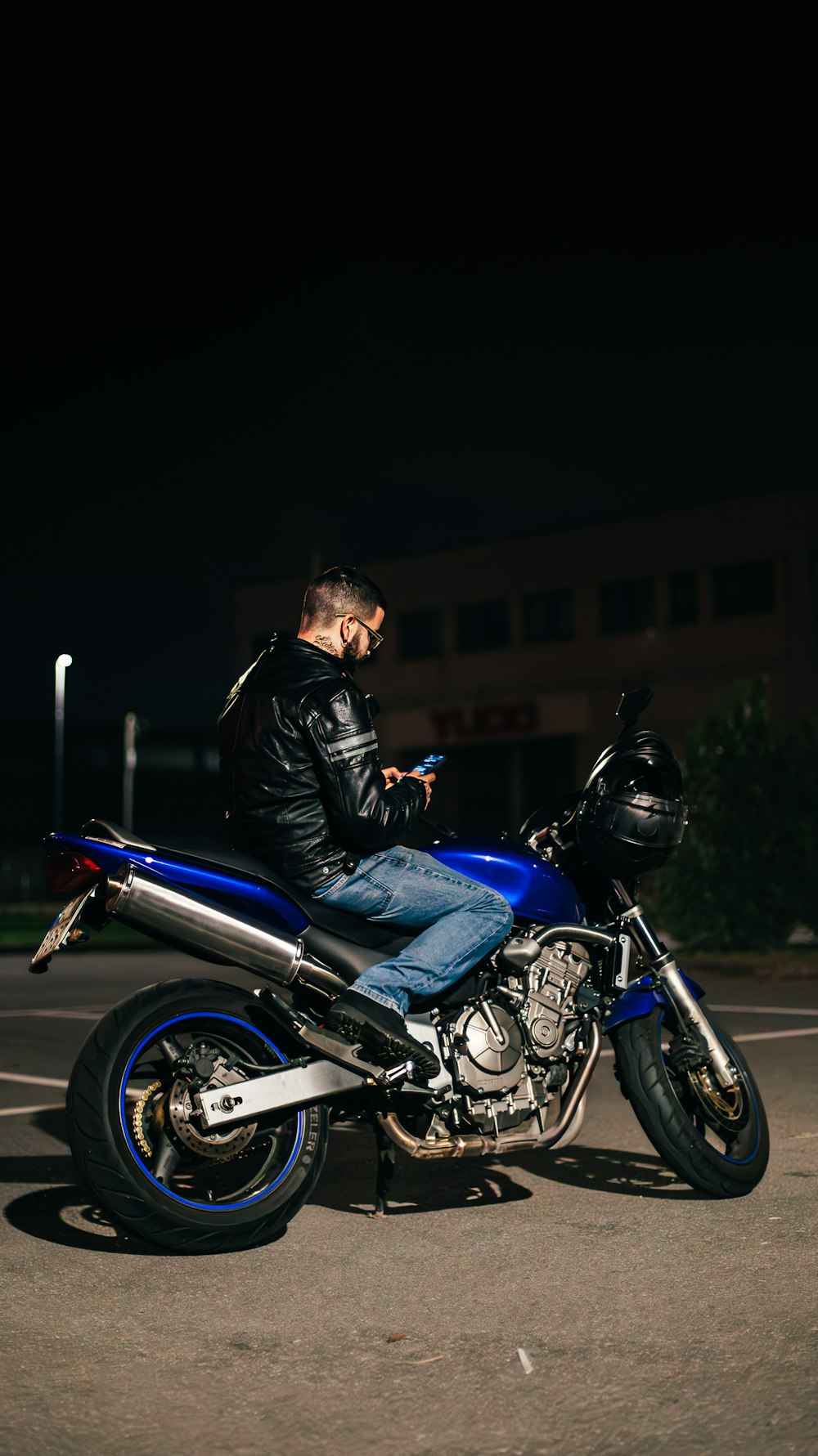 a man sitting on a blue motorcycle in a parking lot