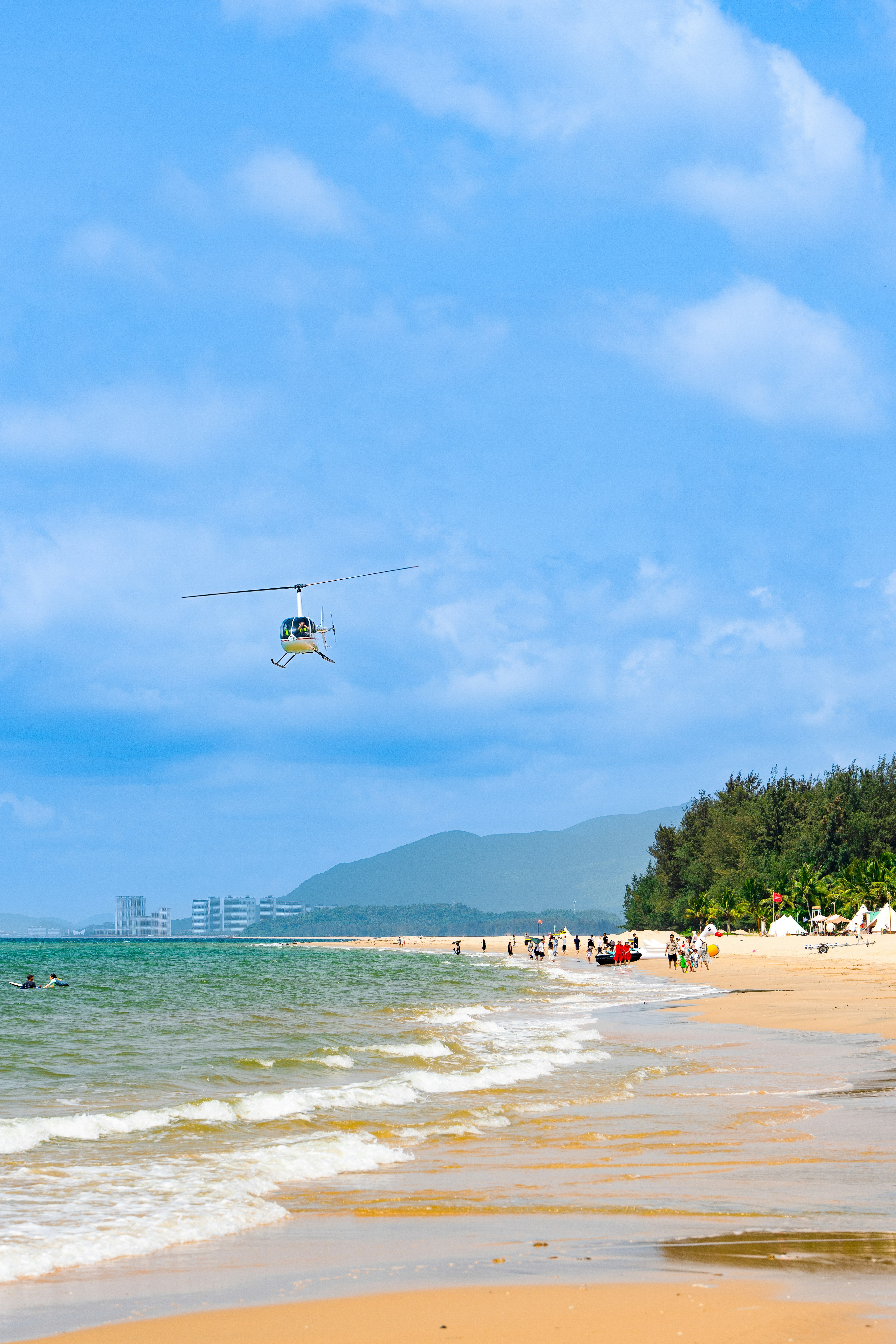 a helicopter flying over a beach with people in the water