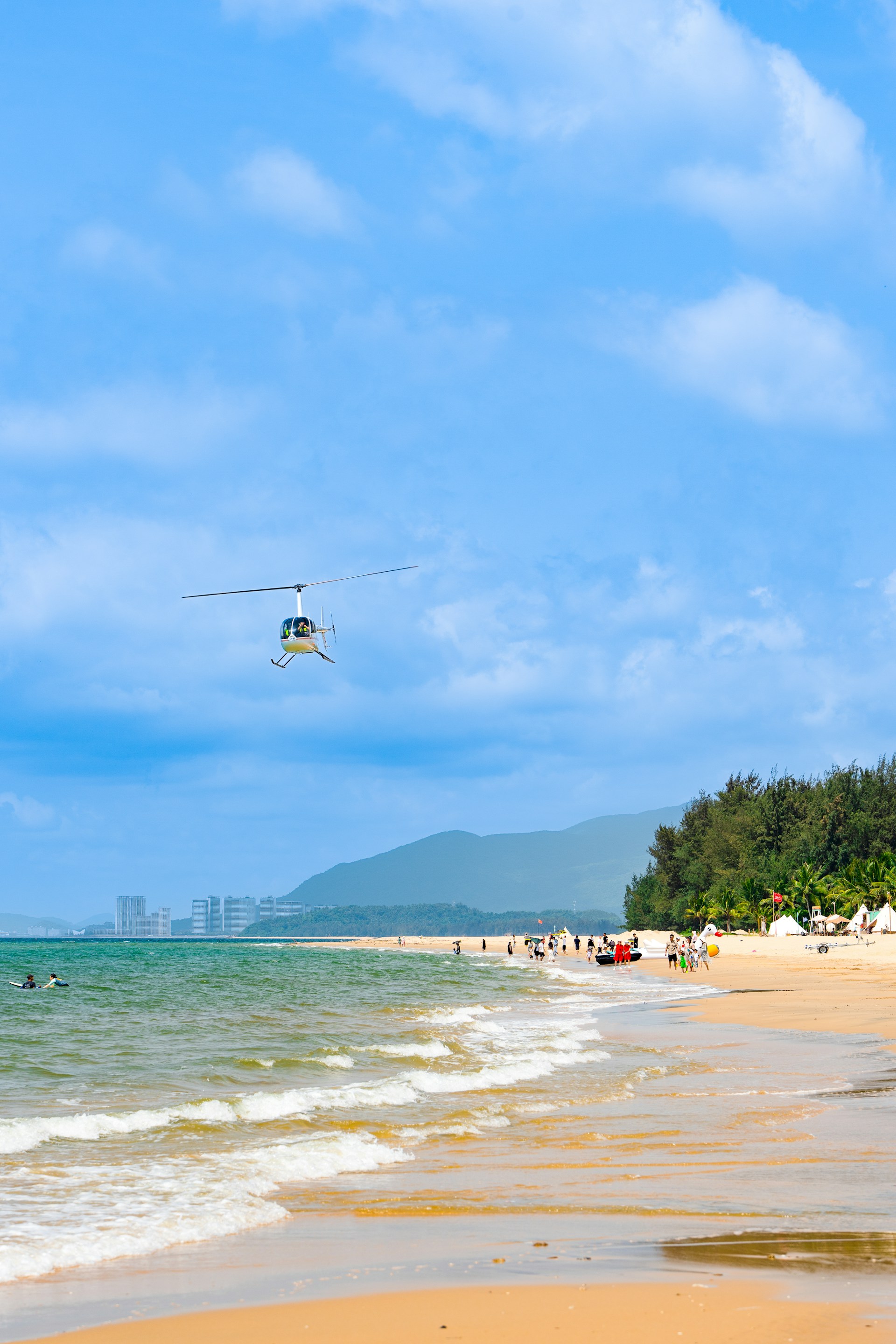 a helicopter flying over a beach with people in the water