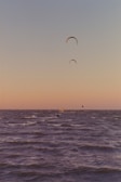 Wide shot of kite surfers riding waves against a vivid sunset sky.