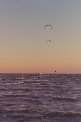Wide shot of kite surfers riding waves against a vivid sunset sky.