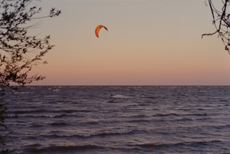 A vibrant kite surfer gliding over the waves at sunset, with colorful kites in the sky.
