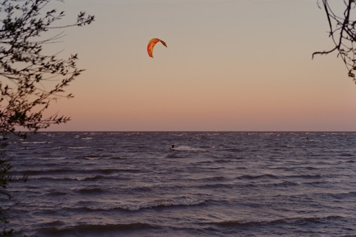 A vibrant kite surfer gliding over the waves at sunset, with colorful kites in the sky.