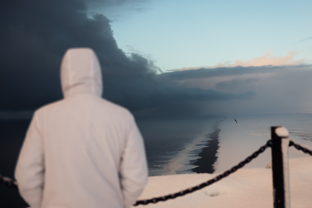 a person in a white jacket looking out at the ocean