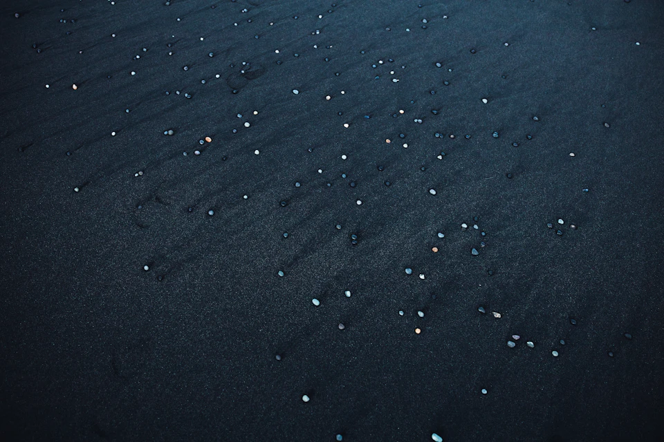 Close-up view of a black sand beach with scattered white specks in aerial perspective