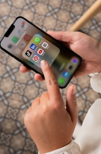 A person is holding a smartphone, displaying a folder of social media apps including TikTok, LinkedIn, WhatsApp, Pinterest, YouTube, and Snapchat. The background consists of a patterned floor.