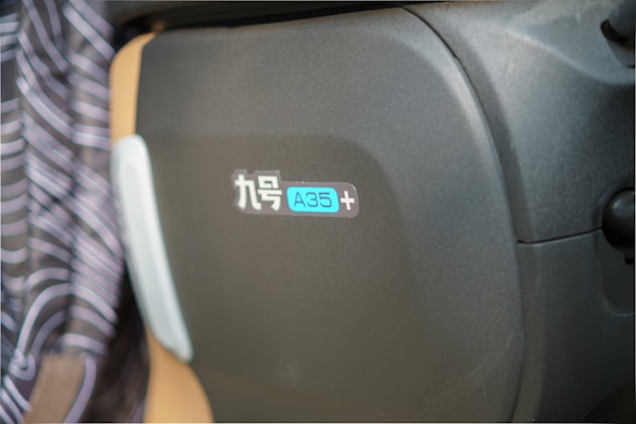 A close-up of a black and beige surface featuring a logo or label in Chinese characters followed by 'A35+'. The background shows part of a striped fabric.