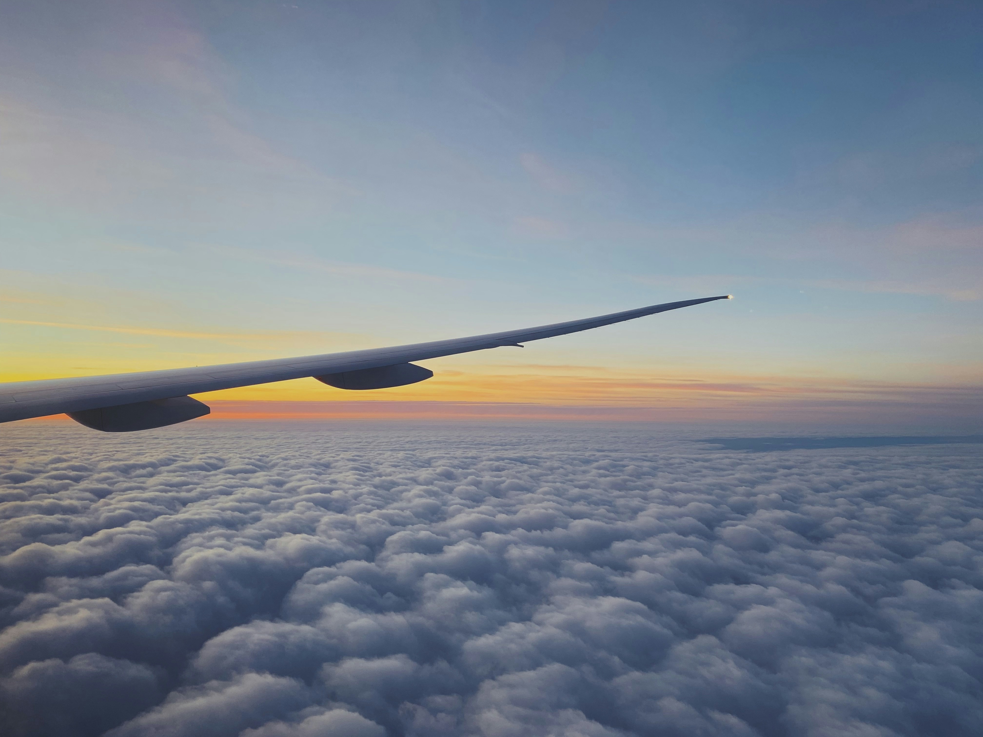 Airplane flying above clouds at sunset, warm orange sky, travel and adventure concept, dark blue horizon