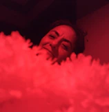 Close-up of a performer’s expressive face illuminated by soft red lighting.