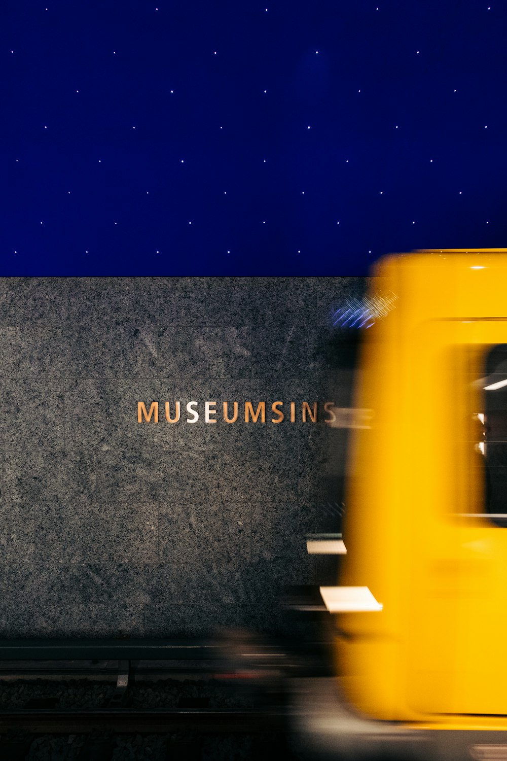 a yellow train traveling past a museum sign