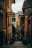 A narrow, picturesque alleyway flanked by colorful buildings with shuttered windows. There are signs for restaurants along the walls, and potted plants add greenery. The alley gently slopes down with cobblestone steps and leads to a scenic view of distant mountains.