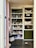 The image features a well-organized storage cabinet filled with a mixture of decorative items, jars, and plush toys. There are glass jars, some with plants, and plush toys resembling animals like reindeer and rabbits. Decorative spider webs are draped across the shelves, giving a hint of a Halloween theme. On one side, a basket and some colorful pet toys are placed on the lower shelves.
