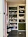 The image features a well-organized storage cabinet filled with a mixture of decorative items, jars, and plush toys. There are glass jars, some with plants, and plush toys resembling animals like reindeer and rabbits. Decorative spider webs are draped across the shelves, giving a hint of a Halloween theme. On one side, a basket and some colorful pet toys are placed on the lower shelves.