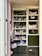 The image features a well-organized storage cabinet filled with a mixture of decorative items, jars, and plush toys. There are glass jars, some with plants, and plush toys resembling animals like reindeer and rabbits. Decorative spider webs are draped across the shelves, giving a hint of a Halloween theme. On one side, a basket and some colorful pet toys are placed on the lower shelves.