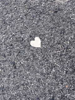 A rough textured asphalt surface with a single, small heart-shaped patch in a contrasting lighter color.